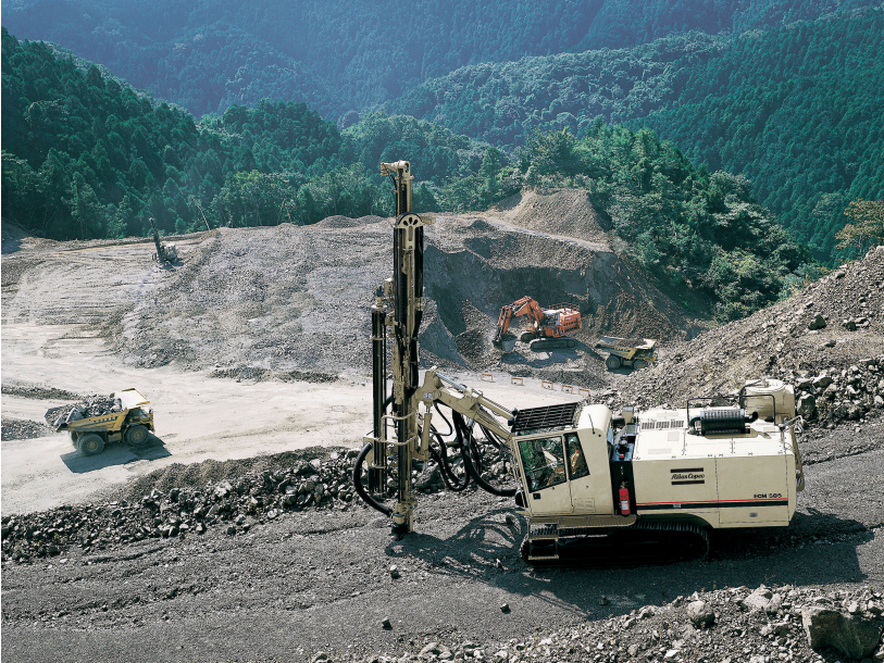 An Atlas Copco surface drill rig operating on a terraced mountainside quarry