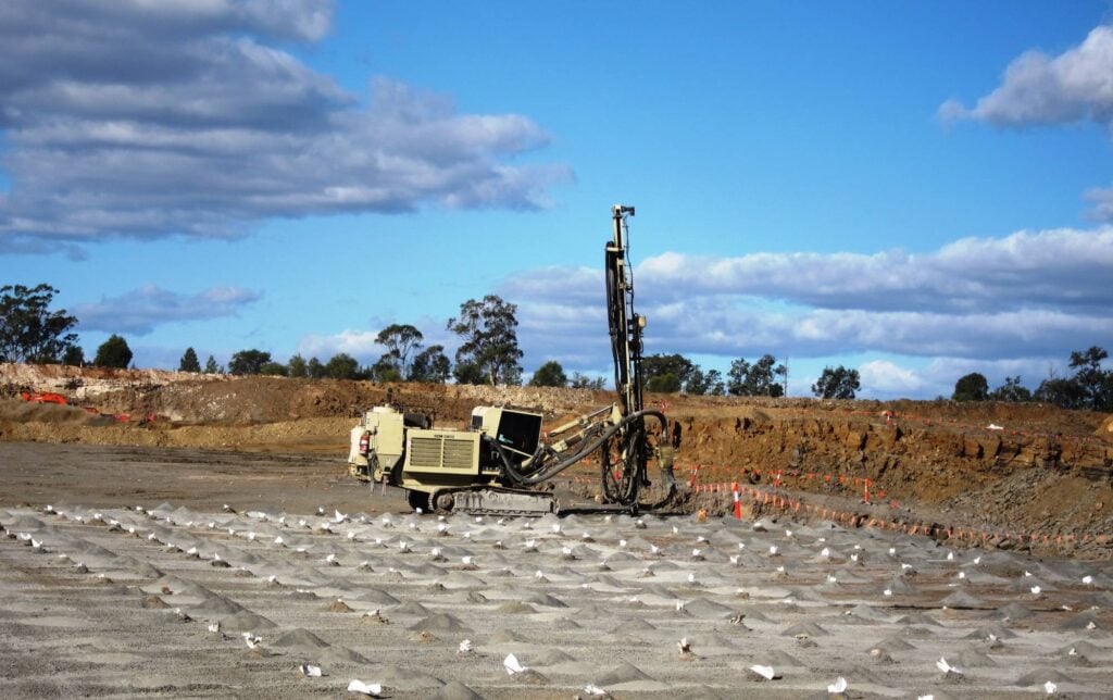 A tan industrial drill rig working on a vast excavation site