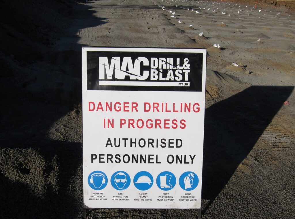 A "MAC Drill & Blast" safety sign at a worksite