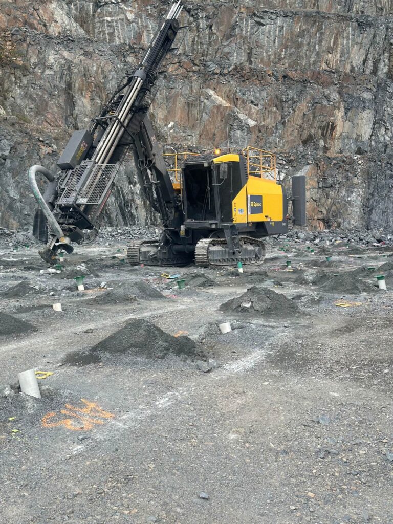 A yellow and grey Epiroc T40 surface drill rig stands in a rocky quarry